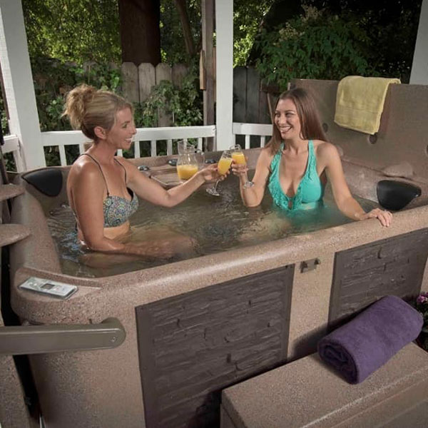 two smiling women holding drinks in hot tub
